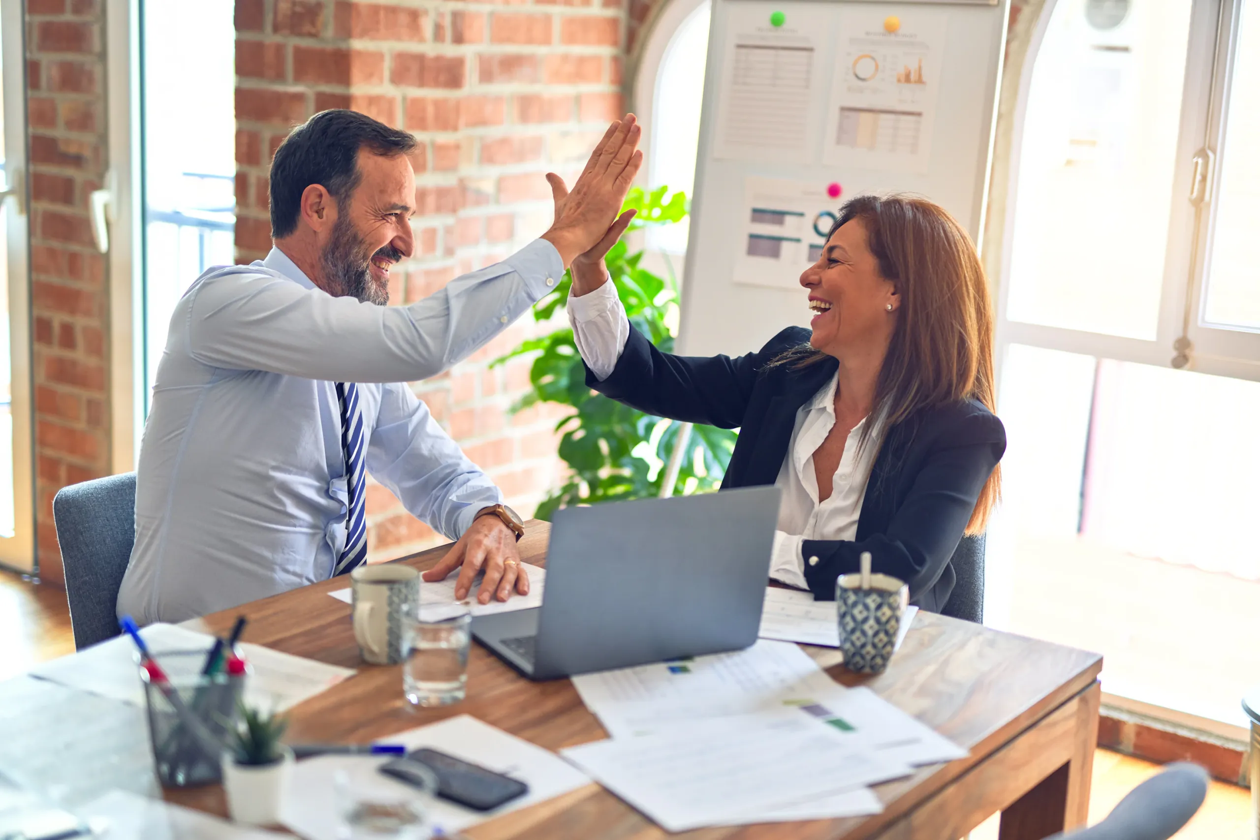 Two colleagues share a high five across an office desk